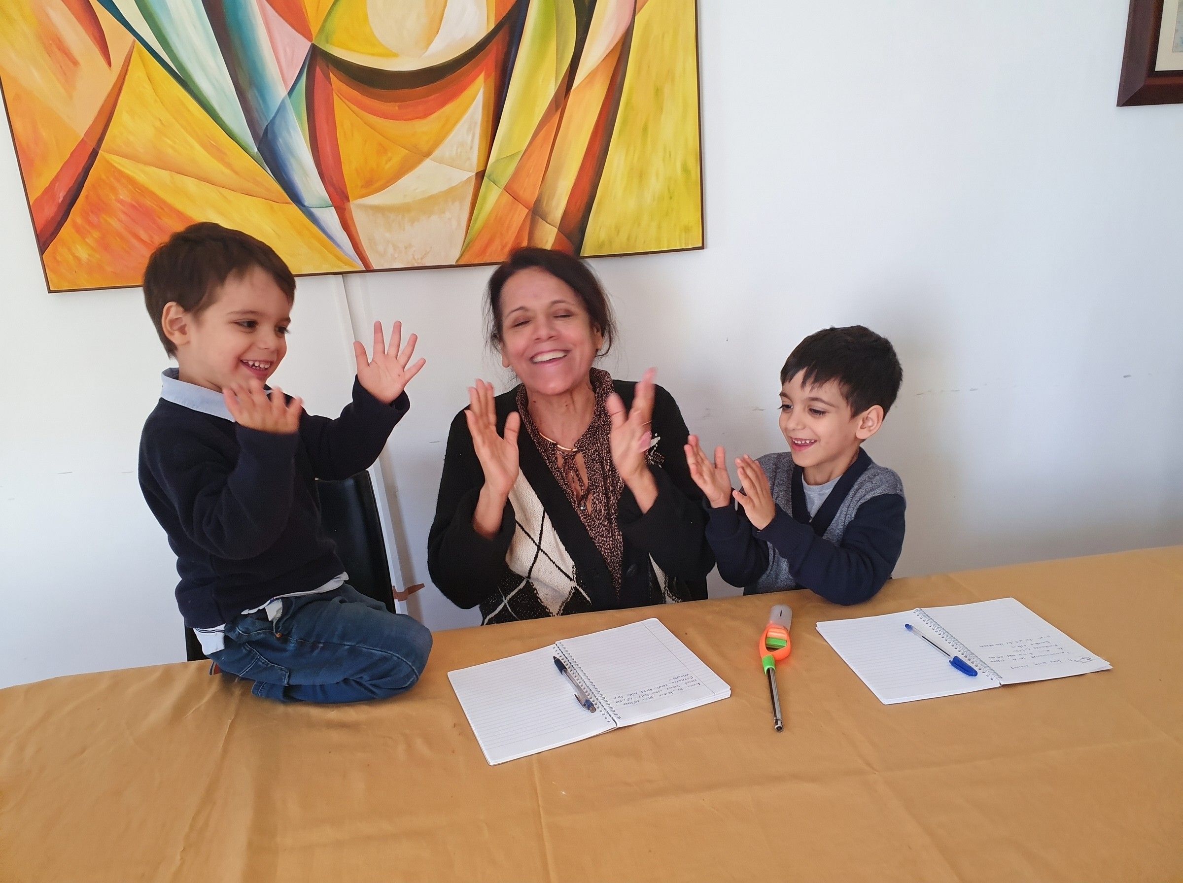 María clapping and laughing with two young children during a Spanish lesson at the table